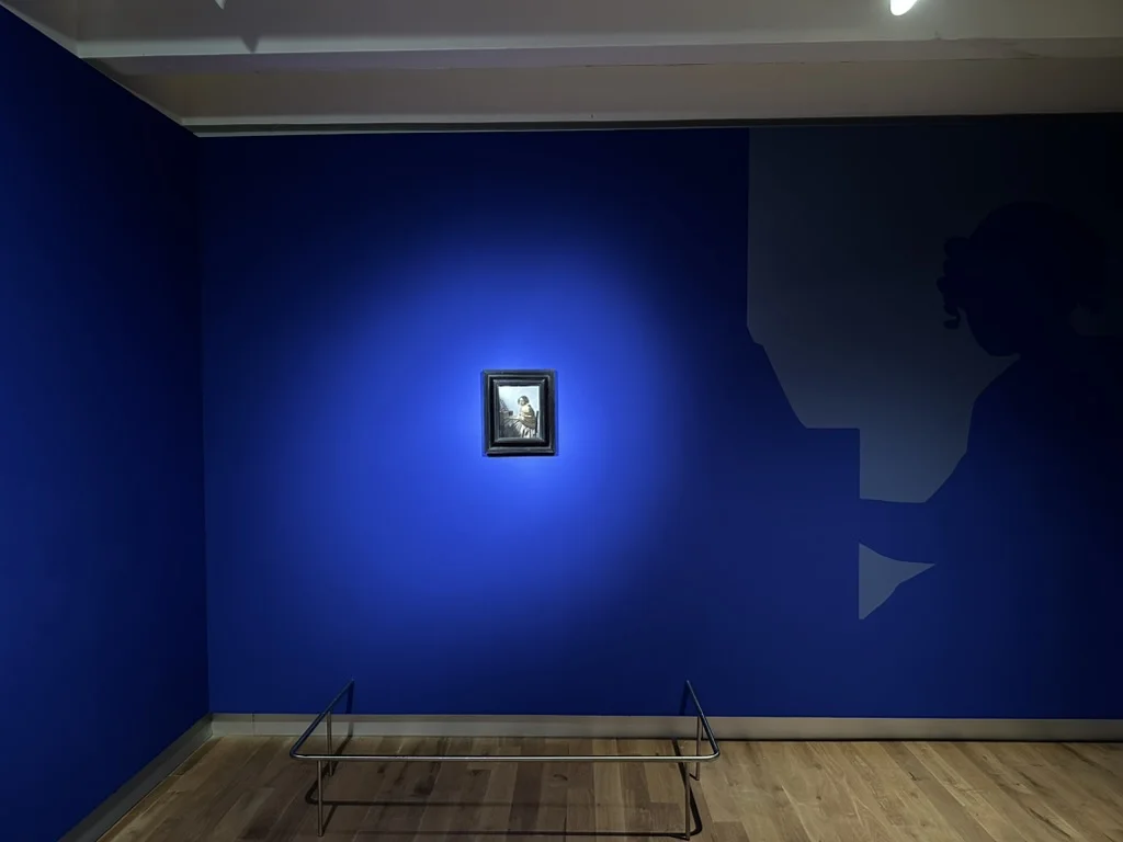 Installation view of Girl with a Pearl Earring at the Nakanoshima Museum of Art, with dramatic lighting and a silhouette graphic on deep blue walls