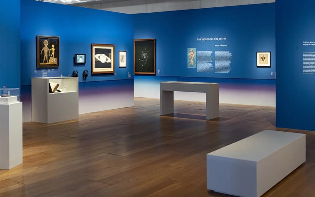 Installation view of Reading the Sky at the MuCEM, with paintings, astronomical displays, and the Les influences des astres wall on deep blue walls