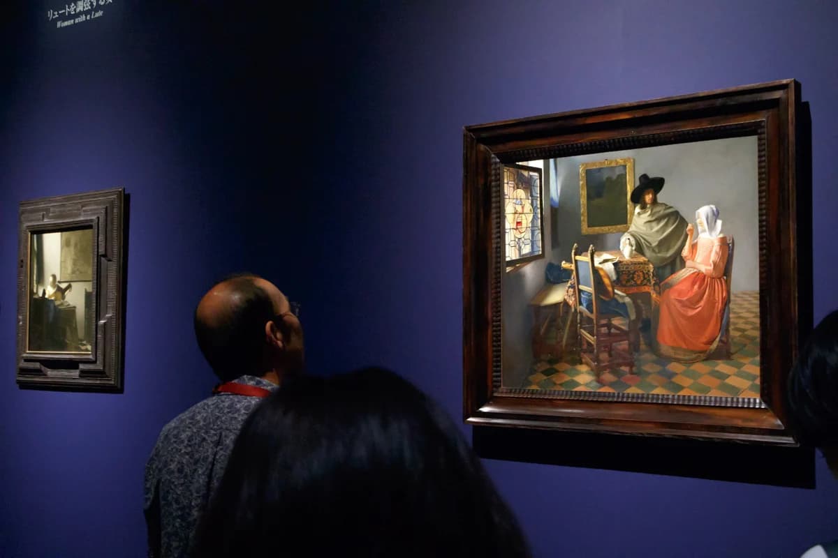 Visitors before The Glass of Wine by Vermeer on a blue wall, with the smaller Woman with a Lute at left