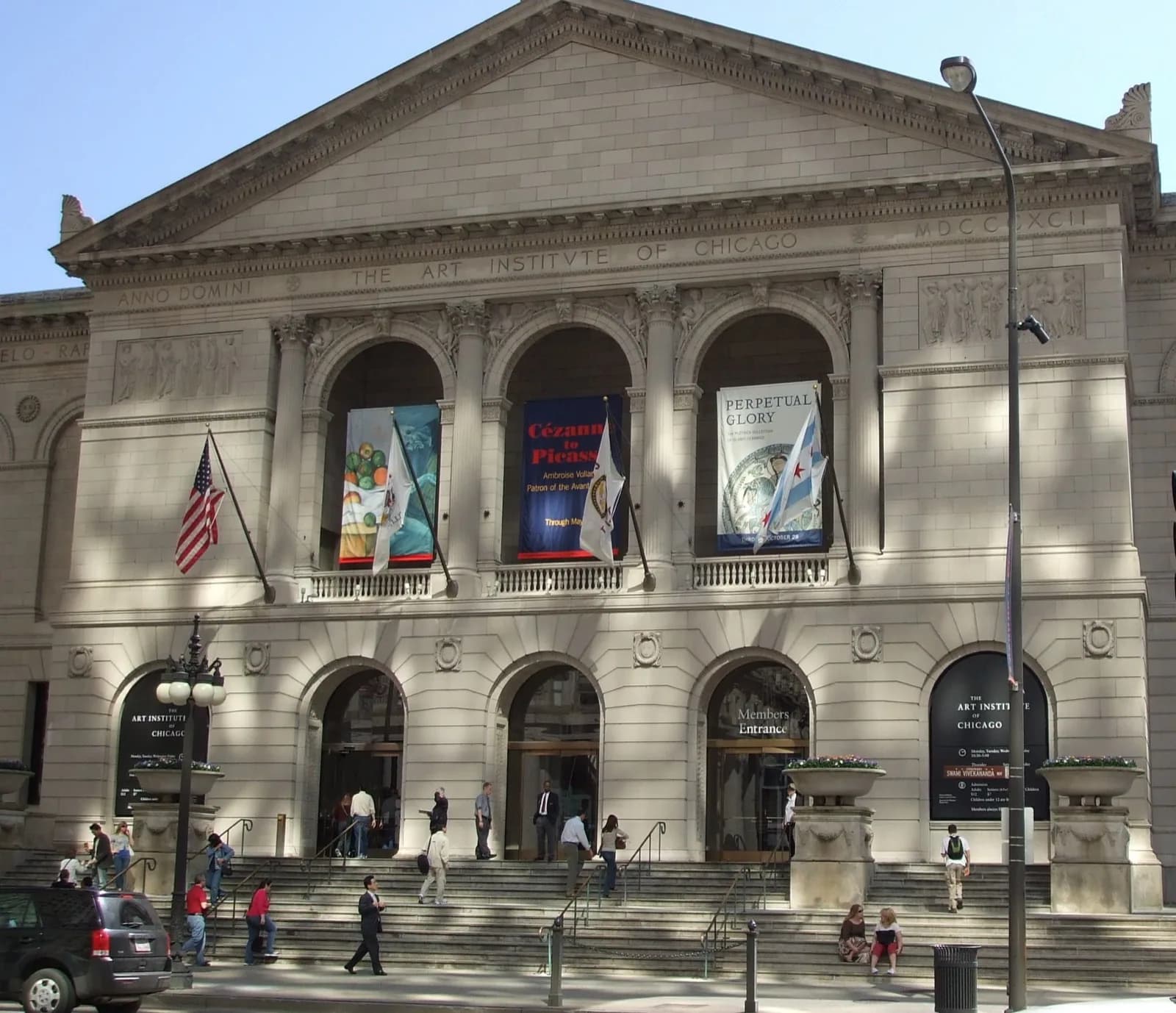 The main building of the Art Institute of Chicago, a grand neoclassical stone building with columns, pediment, and banners, viewed from the street on a sunny day.