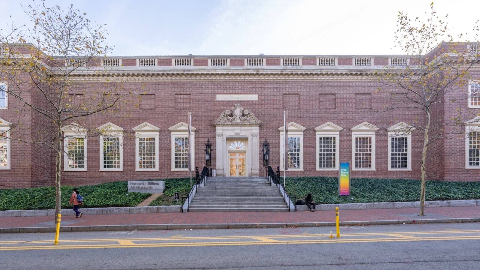 The modern entrance facade of the Harvard Art Museums (Fogg Art Museum) in Cambridge, Massachusetts, featuring glass elements, brick architecture, and the iconic pediment, on a sunny day.