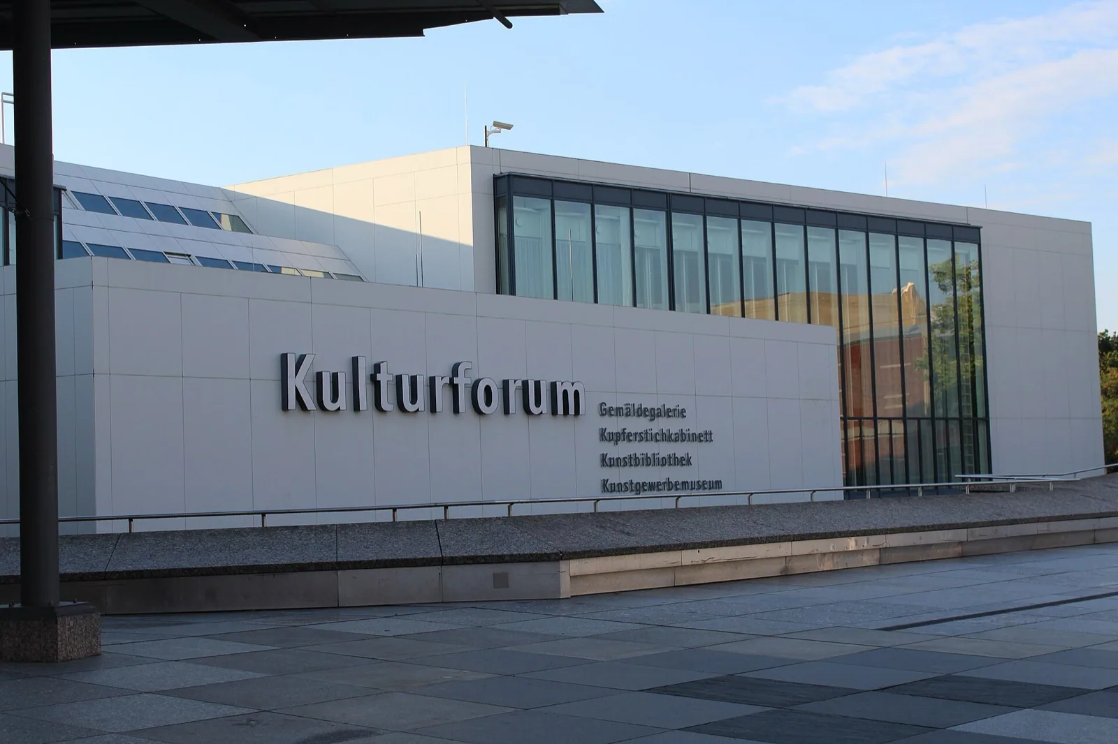 Exterior of the modern Kulturforum complex in Berlin, Germany, housing the Gemäldegalerie, with large white facade, glass windows, plaza and 'Kulturforum' and 'Gemäldegalerie' signage under blue sky.