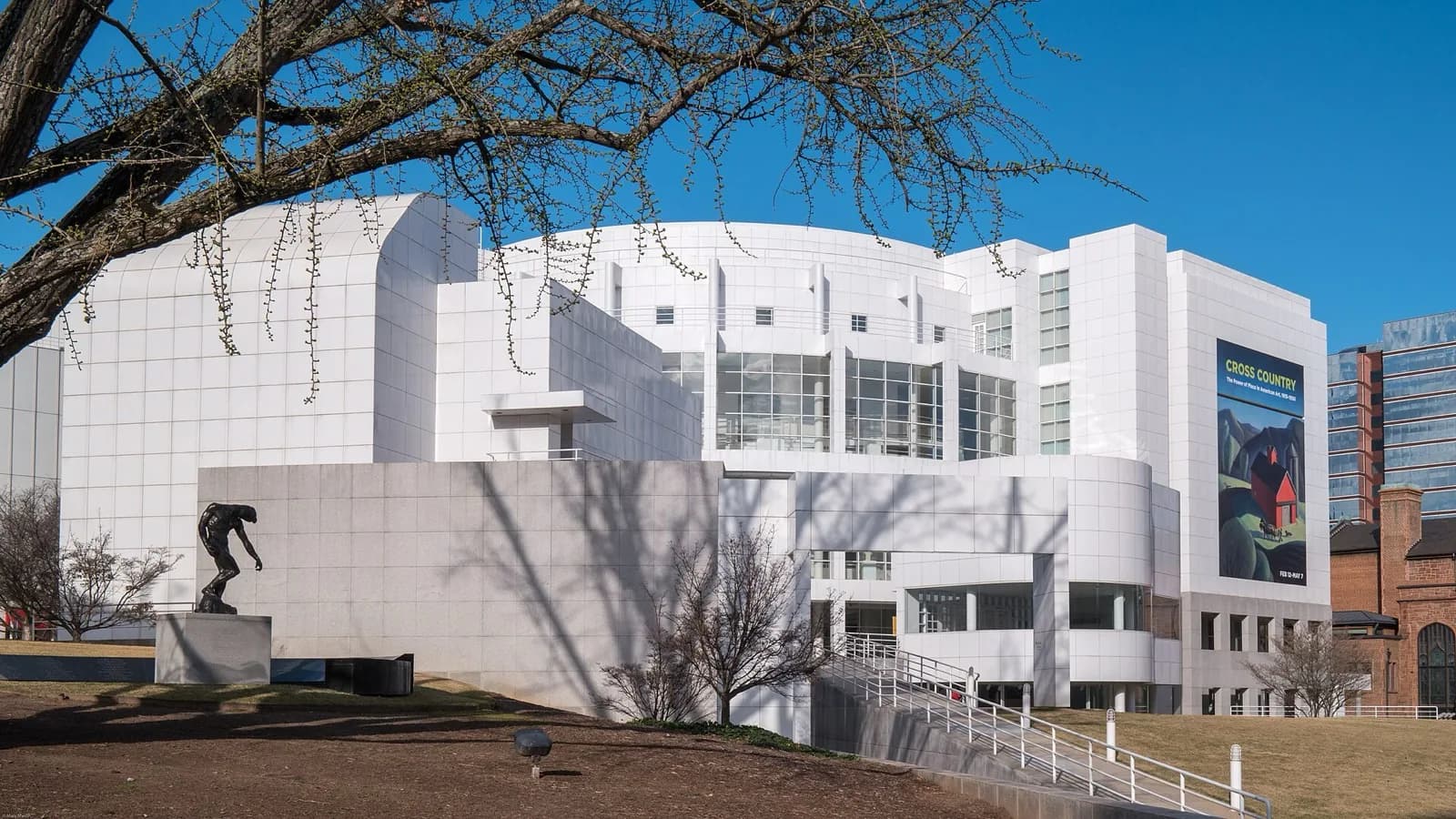 The iconic white modern architecture of the High Museum of Art in Atlanta by Richard Meier, with its curved and angular forms, large windows, and a bronze sculpture by Auguste Rodin in the foreground under a clear blue sky.