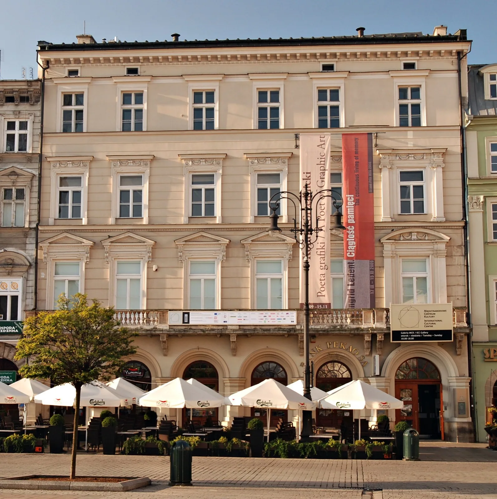 The historic 'Pod Krukami' (Under the Ravens) tenement house on Kraków's Main Market Square, housing the International Cultural Centre, featuring an ornate multi-story facade with arched windows, balconies, decorative elements and an 'MCK' sign under a clear blue sky.