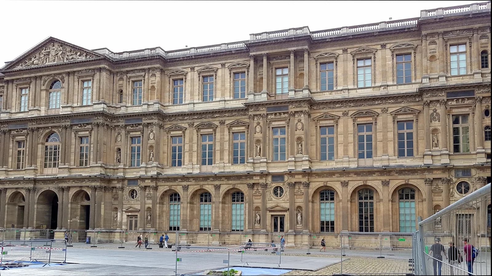The historic ornate stone facade of the Palais du Louvre in Paris, with classical architecture, columns, pediments, and numerous sculptures in the Cour Carrée.