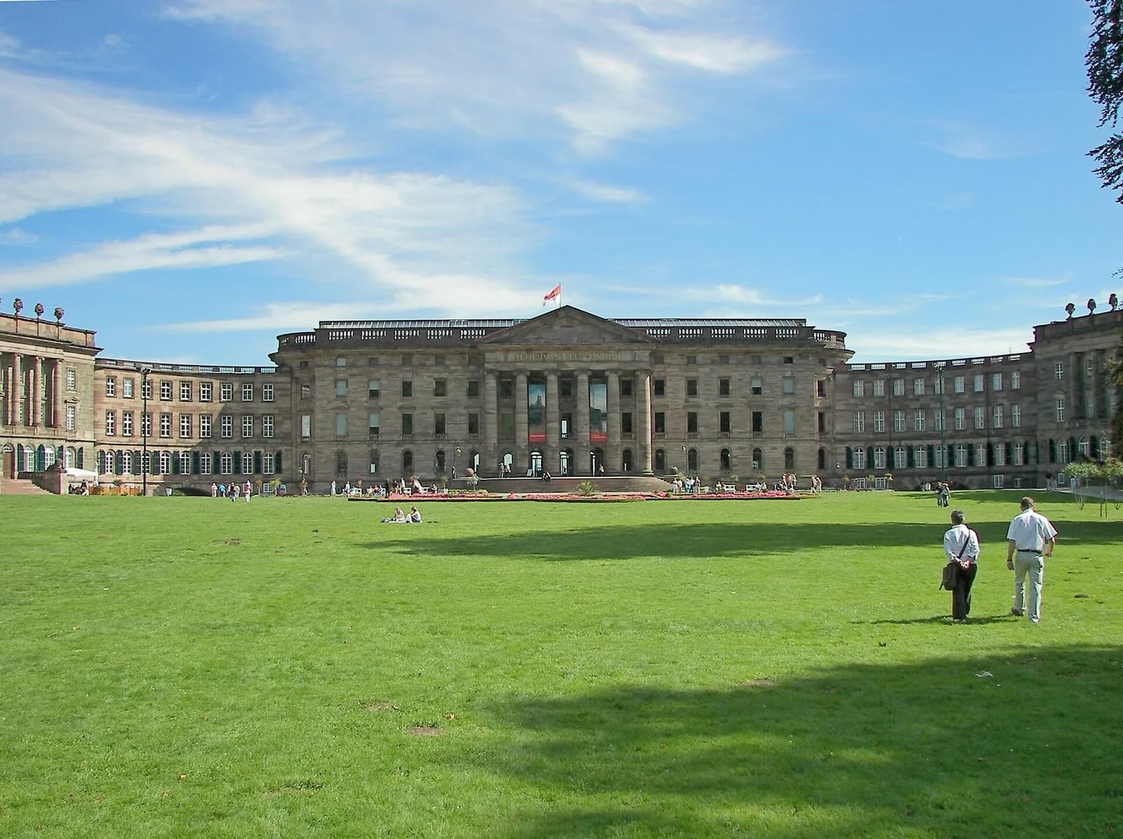 The grand baroque Schloss Wilhelmshöhe palace in Kassel, home to collections of the Museumslandschaft Hessen Kassel, featuring its central tower, symmetrical wings, and formal gardens with fountains under a blue sky.
