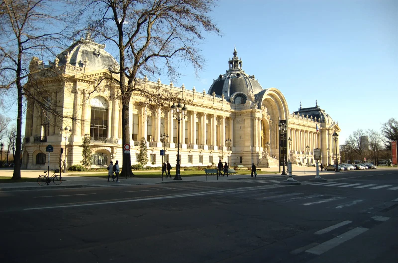 The ornate Beaux-Arts stone facade of the Petit Palais in Paris, featuring grand columns, pediments, allegorical sculptures, and a large arched entrance with dome above, on Avenue Winston-Churchill.