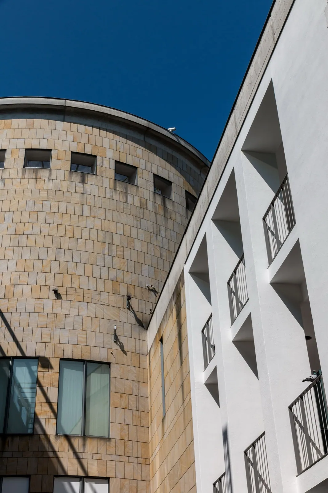 Low-angle view of the curved stone facade and white geometric concrete structure of the Schirn Kunsthalle in Frankfurt, Germany, under a clear blue sky.
