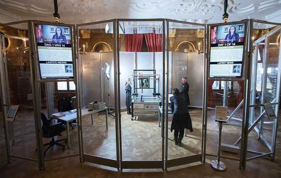 The painting on a horizontal scanning bridge inside a glass-walled enclosure in the Mauritshuis Golden Room, with researchers working and screens reporting the day's findings
