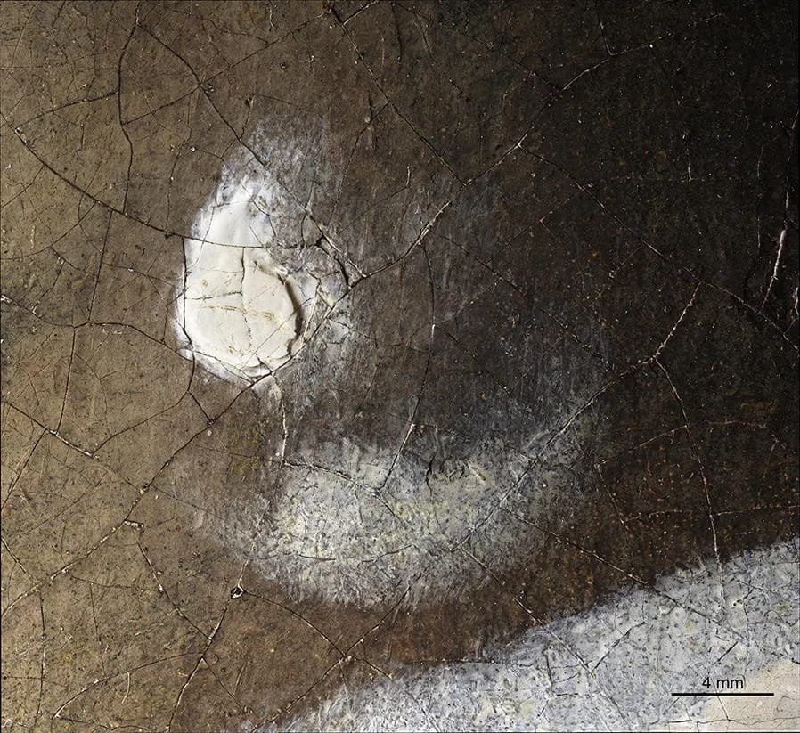 The pearl earring at 140x magnification: a thick teardrop of white impasto at the upper left and a soft, paler gleam below it, over a dark cracked ground