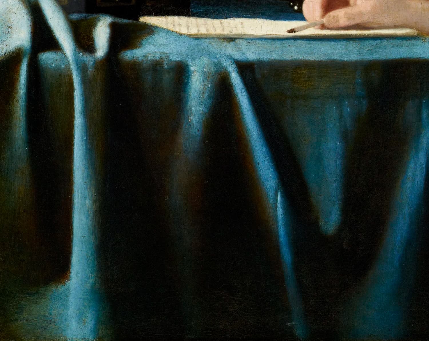 Detail of the blue tablecloth in Mistress and Maid, its folds catching the light, with the edge of the letter and the mistress's hand above